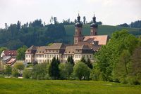 Blick auf die Kirche St. Peter mit dem ehemaligen Benediktiner-Kloster liegend zwsichen grünen Wiesen und vor den Hügeln des Schwarzwaldes.