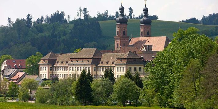 Blick auf die Kirche St. Peter mit dem ehemaligen Benediktiner-Kloster liegend zwsichen grünen Wiesen und vor den Hügeln des Schwarzwaldes.