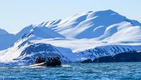 Eine Gruppe Menschen fährt in einem Zodiac Boot vor einem schneebedeckten Berg im Magdalenenfjord.