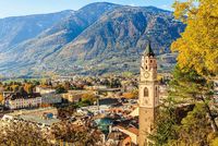 Herbstlicher Blick über die Altstadt von Meran mit Stadtturm, bunten Bäumen und der umliegenden Berglandschaft Südtirols im goldenen Herbstlicht.