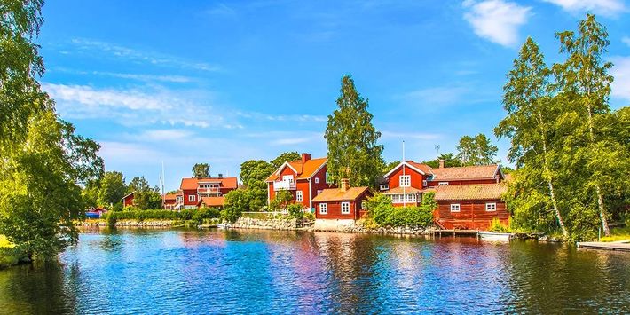 Rote Holzhäuser spiegeln sich im ruhigen Wasser – eine Bilderbuchlandschaft, die das ursprüngliche Schweden mit Seen, Wäldern und traditioneller Architektur erlebbar macht. | Foto: Margit-Kluthke/AdobeStock