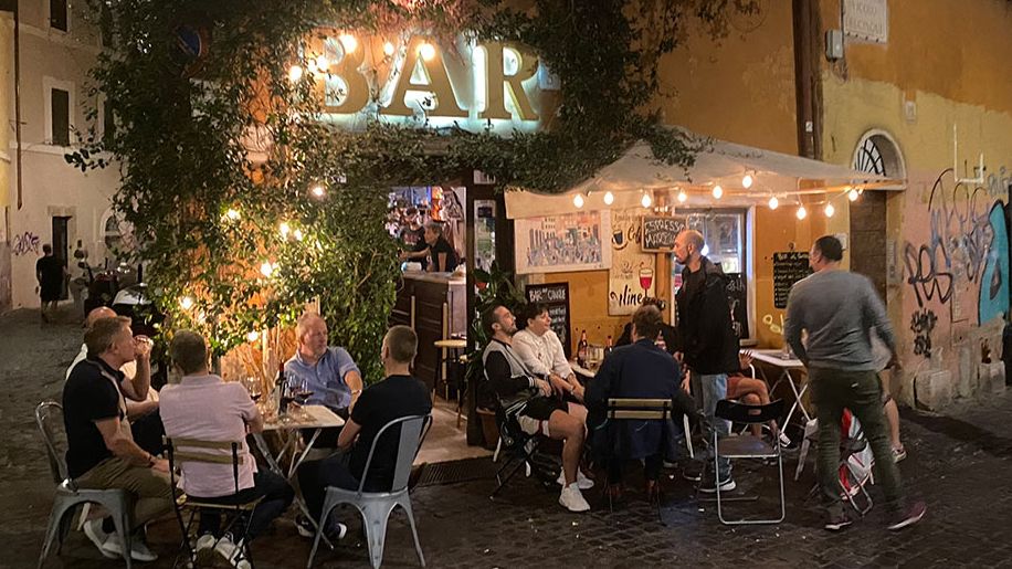 Vor einer Bar im römischen Stadtteil Trastevere lassen einige Menschen gemnütlich den Tag bei  einem Glas Wein ausklingen.