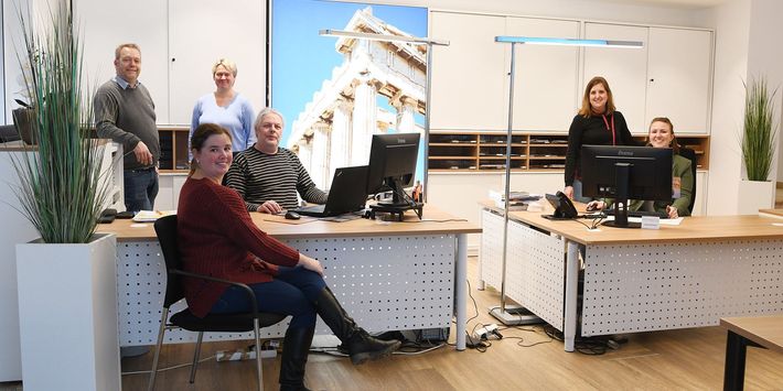 Das Team von Emmaus-Reisen hat sich um die Schreibtische im Büro und Verkaufsraum aufgestellt.