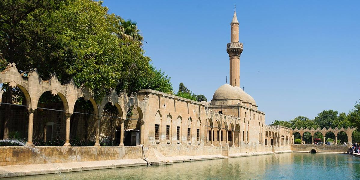 Historische Fischteiche (Balıklıgöl) in Şanlıurfa mit Moschee, Arkadengängen und Wasserbecken unter blauem Himmel