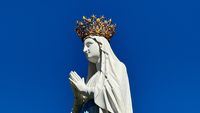 Gekrönte Marienstatue an der Erscheinungsgrotte von Lourdes vor blauem Himmel – Pilgerziel des berühmten Wallfahrtsortes in Südfrankreich.