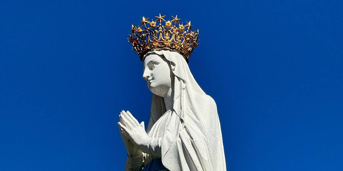 Gekrönte Marienstatue an der Erscheinungsgrotte von Lourdes vor blauem Himmel – Pilgerziel des berühmten Wallfahrtsortes in Südfrankreich.