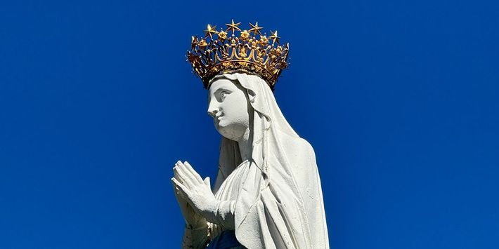 Gekrönte Marienstatue an der Erscheinungsgrotte von Lourdes vor blauem Himmel – Pilgerziel des berühmten Wallfahrtsortes in Südfrankreich.