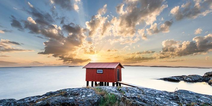Eine rote Holzhütte steht auf einem Felsen am Meer.