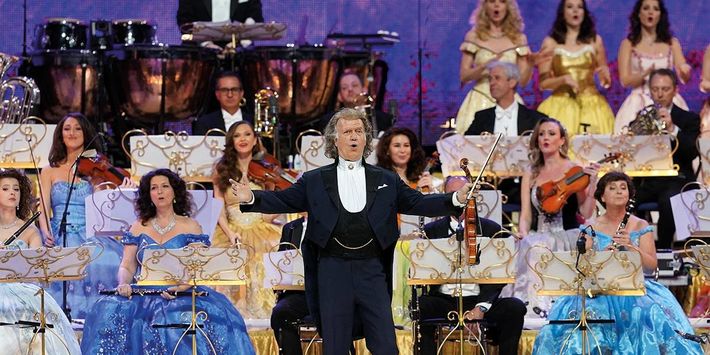 André Rieu mit Geige in der Hand inmitten eines Orchesters auf der Bühne.