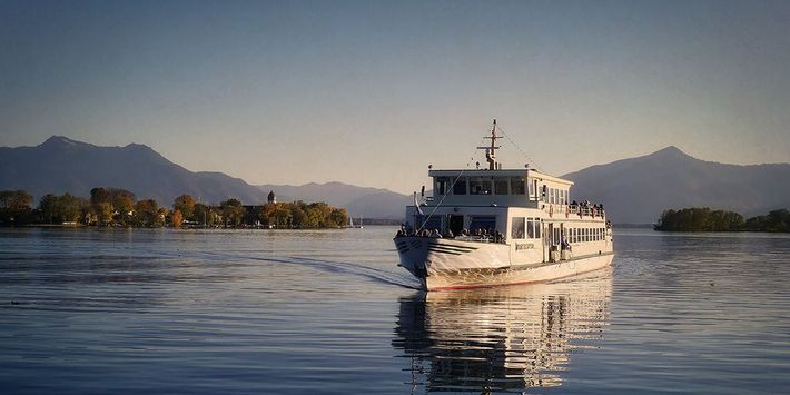 Ein Ausflugsschiff fährt über den Chiemsee, im Hintergrund liegen die Alpen.